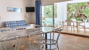 Una habitación con un sofá a cuadros, una mesa de comedor con sillas, un televisor montado en la pared y vistas al exterior a través de una puerta corredera.