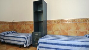 Una habitación con dos camas, cada una con ropa de cama a rayas, una alta estantería de color oscuro y una pared de azulejos con un borde decorativo.