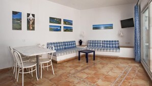 Una sala de estar con un sofá, una mesa de comedor con sillas y un televisor montado en la pared.