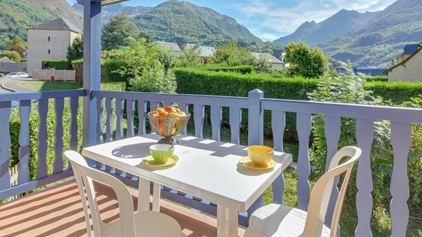 A balcony with a table and chairs, overlooking a mountainous landscape.