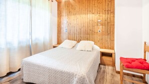 Un dormitorio con techo de madera, una cama con colcha estampada, una mesita de noche, una silla roja y un panel de pared de madera.