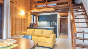 Un interior de madera con un sofá amarillo, una mesa de comedor y una zona de cocina con armarios y un microondas.