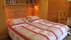 Une chambre confortable avec un lit, des murs en bois, une chaise et une étagère contenant des livres et une petite figurine.