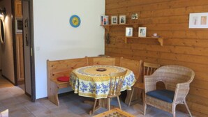 Un coin repas chaleureux avec une table et des chaises en bois, une horloge au mur et une étagère où sont exposés des tableaux encadrés.