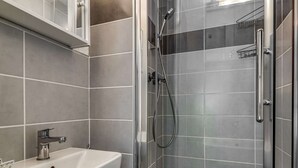 Un bagno con un lavandino bianco, una cabina doccia in vetro e piastrelle grigie.