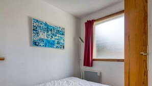 Una camera da letto con un letto bianco, un poster floreale blu al muro, una finestra con tenda rossa e una porta di legno.