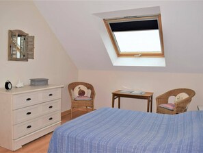 A bedroom with a skylight, a bed, a dresser, two wicker chairs, and a small table.