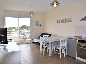 A modern kitchen with a dining table, chairs, and a dishwasher. There is a large window with a view of the outside. - 3* Apartment with elevator, balcony and private parking in Trégastel (Trégastel)