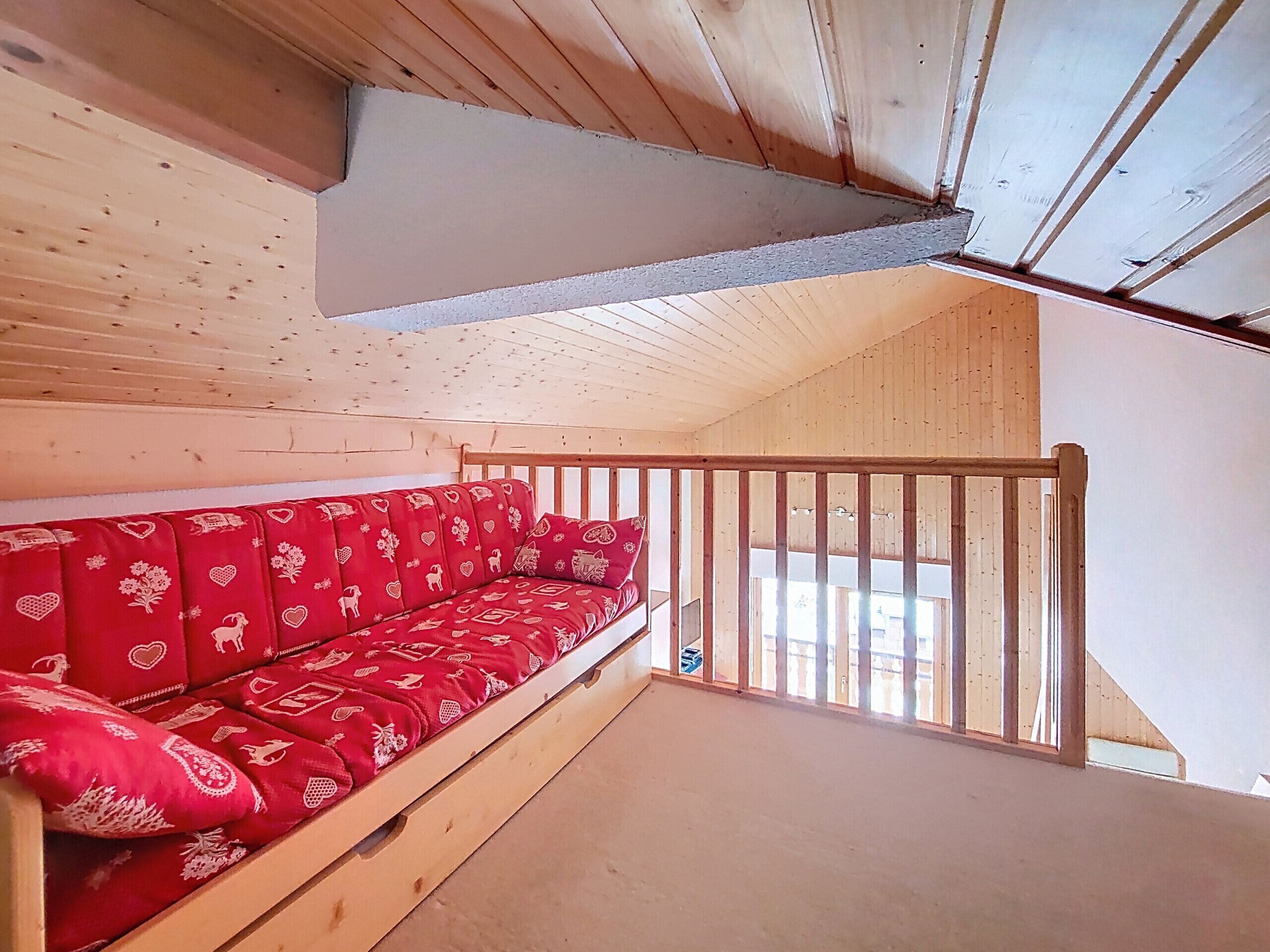 A wooden loft bedroom with a red sofa and a wooden railing.