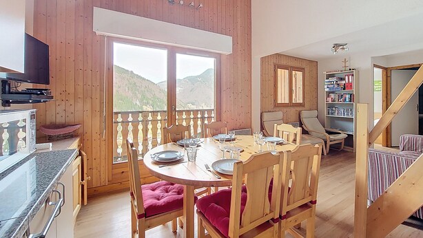 A dining area with a wooden table and chairs, a television, and a bookshelf.