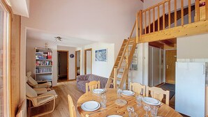 A dining area with a wooden table set for four, a staircase, and a kitchen area with a refrigerator.