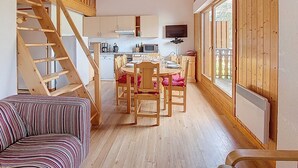 A cozy cabin interior with a wooden staircase, a dining area with a table and chairs, and a kitchen with modern appliances.