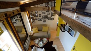 A compact living space with a loft bed, a sofa, a dining area, and a wall adorned with framed pictures. - E5GG Honey Mustard (París)