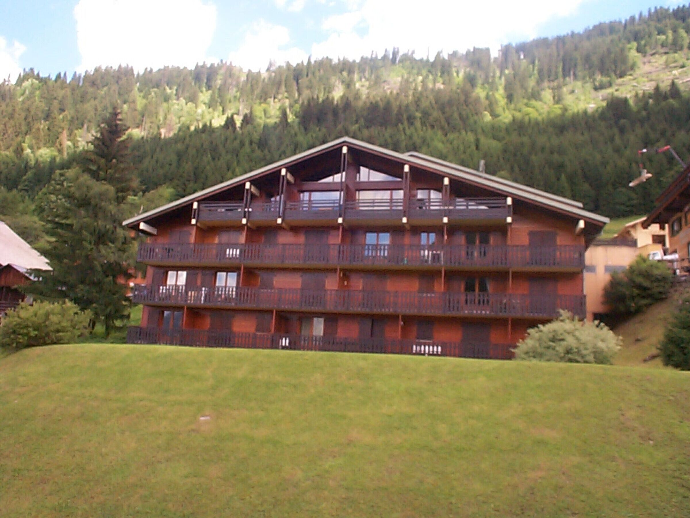 A multi-story building with balconies, set against a mountainous backdrop.