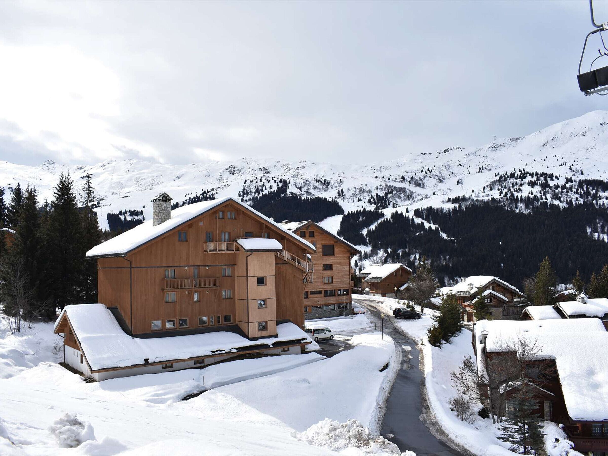 A wooden lodge with multiple floors and balconies, surrounded by snow-covered mountains and a ski lift.