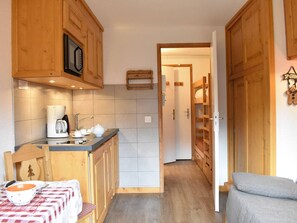 A compact kitchen with wooden cabinets, a coffee machine, and a table with a checkered tablecloth. - Charming Renovated Studio for 3 Near Slopes with Balcony in Méribel (Méribel)