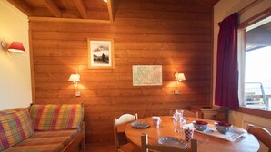 A cozy room with wooden walls, a round wooden table with chairs, a colorful sofa, and two wall-mounted lamps. - 2 rooms + mezzanine in Valmorel, 5 pax, balcony, linens and cleaning included (Valmorel)