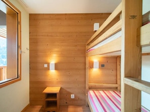 A compact room with wooden walls, a small wooden bench, and a bunk bed with a striped bedspread.