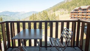 A balcony with a table and two chairs, overlooking a mountainous landscape and a lodge building. - 2 rooms + mezzanine in Valmorel, 5 pax, balcony, linens and cleaning included (Valmorel)