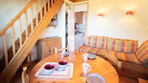 A cozy room with a wooden staircase, a dining table with plates and cups, a colorful sofa, and a kitchen area. - 2 rooms + mezzanine in Valmorel, 5 pax, balcony, linens and cleaning included (Valmorel)