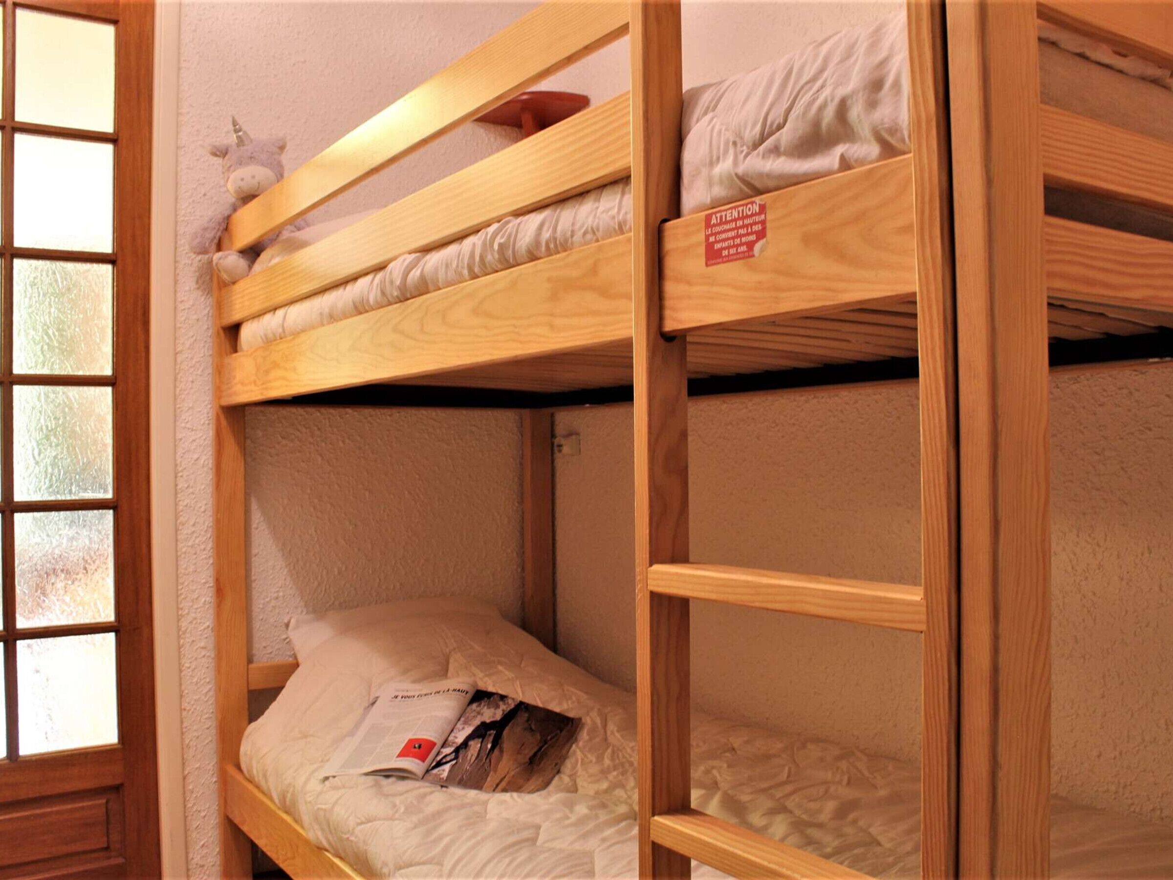A bunk bed with a wooden frame, a plush toy on the top bunk, and a pillow on the bottom bunk.