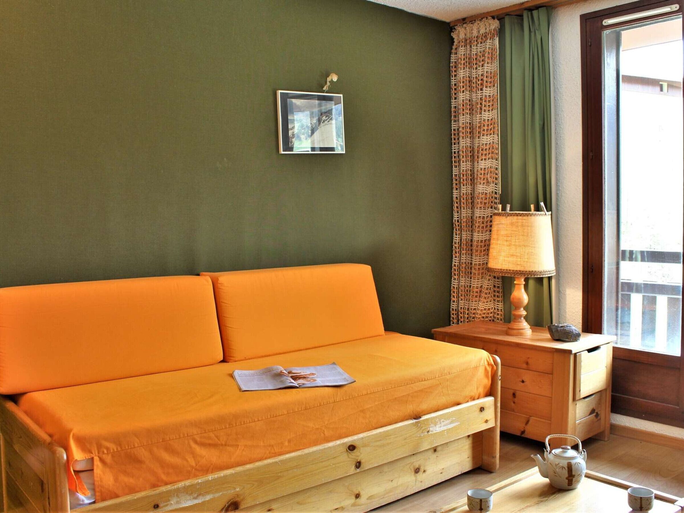 Una stanza con un letto di legno, un comodino in legno, una lampada e una finestra con tende.