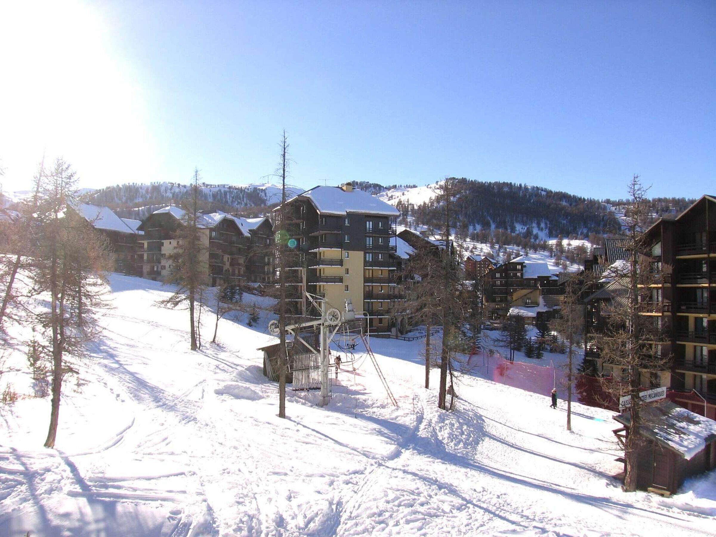 A snow-covered ski resort with multi-story buildings, ski lifts, and a mountainous backdrop.