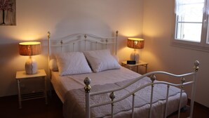 A neatly made bed with white bedding, two bedside lamps, and a small bedside table with a phone.