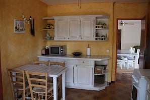 A compact kitchen with white cabinets, a microwave, and a dining area with a table and chairs.