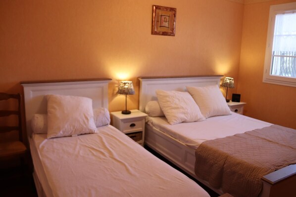 Habitación de hotel con dos camas individuales, mesitas de noche con lámparas, una mesita auxiliar con un reloj y una ventana con vistas.