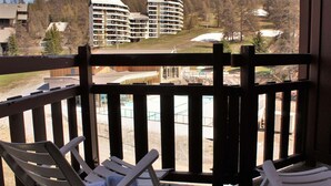 A balcony with two white chairs, overlooking a pool area and a view of multi-story buildings in a forested area. - 2-room apartment for 4 - Ski-in/ski-out, summer pool (Risoul)