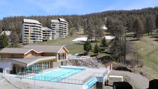 A resort with a pool area, multiple buildings, and a forested hillside in the background. - 2-room apartment for 4 - Ski-in/ski-out, summer pool (Risoul)