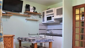 A compact kitchen with a dining table, wooden benches, a microwave, and a television on a shelf. - 2-room apartment for 4 - Ski-in/ski-out, summer pool (Risoul)