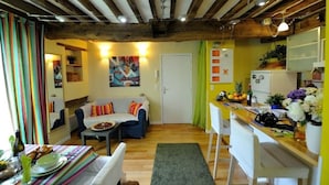 A cozy living room with a sofa, a dining table with chairs, and a kitchen area with a refrigerator and a sink. - B3DD Honeymoon (París)