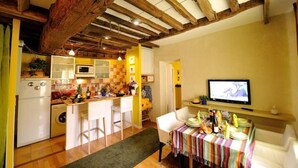 A cozy kitchen with a wooden ceiling, a dining area with a colorful tablecloth, and a television on the wall. - B3DD Honeymoon (París)