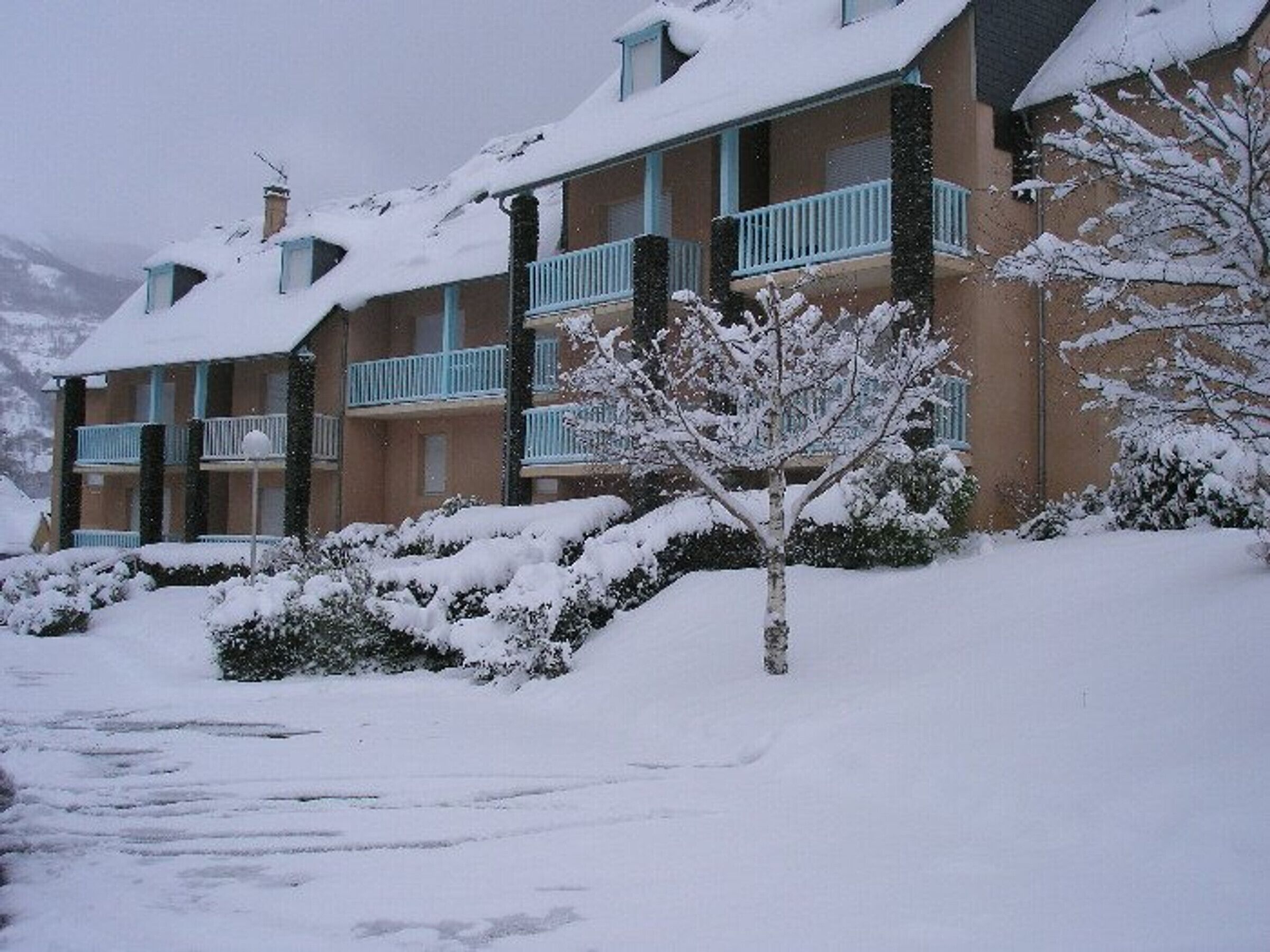 A multi-story building with balconies, surrounded by snow-covered ground and trees.
