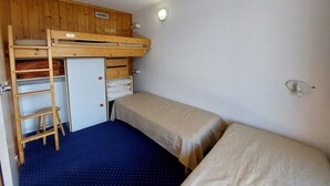 Una habitación pequeña y funcional con una cama litera, un escritorio y una escalera.
