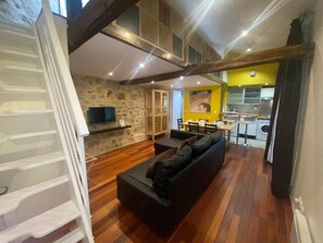 A modern living room with a black sofa, wooden flooring, a stone wall, and a kitchen area with a yellow accent wall. - F1G Niagara (París)