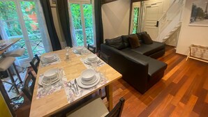 A dining area with a wooden table set for four, a black sofa, and a staircase leading to an upper level.