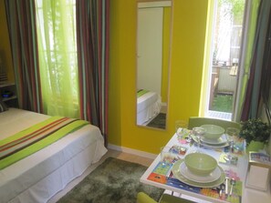 Une chambre d’hôtel avec un lit, une table à manger dressée avec des assiettes, des verres et un saladier vert.