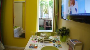 A dining area with a table set for two, a TV mounted on the wall, and a window with a view of the outside. - E1GG Everglades (Paris)