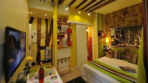 A cozy hotel room with a bed, a TV, a table with a bottle and glasses, and a city view through a window. - E1GG Everglades (Paris)