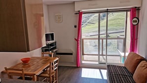 Una sala de estar acogedora con una mesa de madera, sillas, un sofá y un televisor sobre un mueble.
