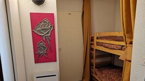 Una habitación pequeña con una cama alta, un adorno rojo en la pared y una rejilla blanca.