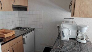Una cocina compacta con estufa a gas, cafetera y hervidor sobre la encimera.