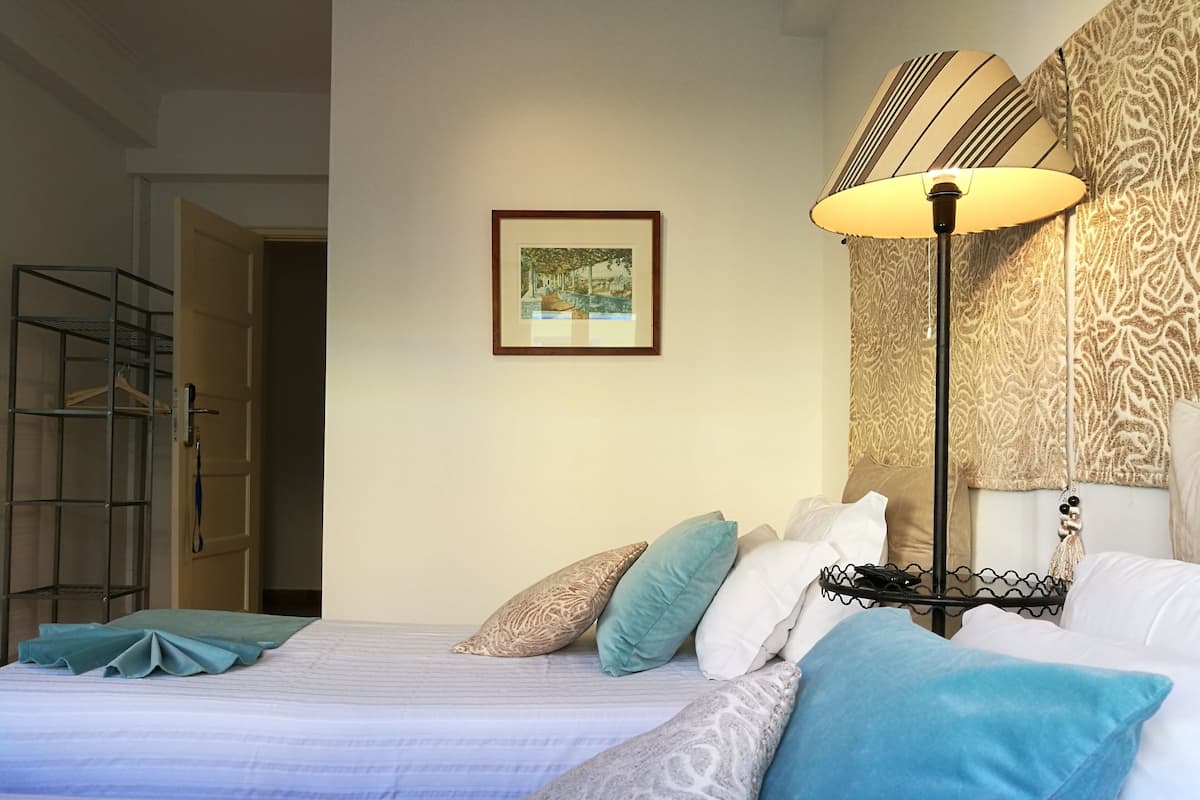 Een netjes ingerichte slaapkamer met een bed, kussens, een vloerlamp, een ingelijst foto op de muur en een garderobe met hangers.