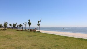 Una playa con cielo despejado, una orilla arenosa y un puente a lo lejos.