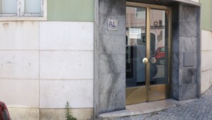 Entrada de un edificio con puerta de cristal, un pequeño letrero encima de la puerta y el número '6' en la pared.