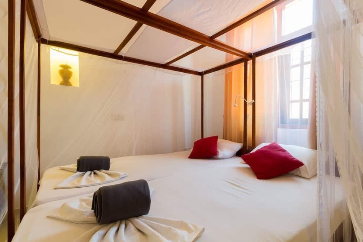 Ein Hotelzimmer mit einem Himmelbett, einem Fenster mit Vorhängen und einem Nachttisch mit einer Lampe.