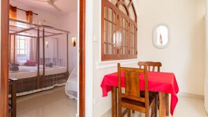 Une chambre à coucher avec un lit à baldaquin, une table à manger recouverte d’une nappe rouge et une chaise en bois.
